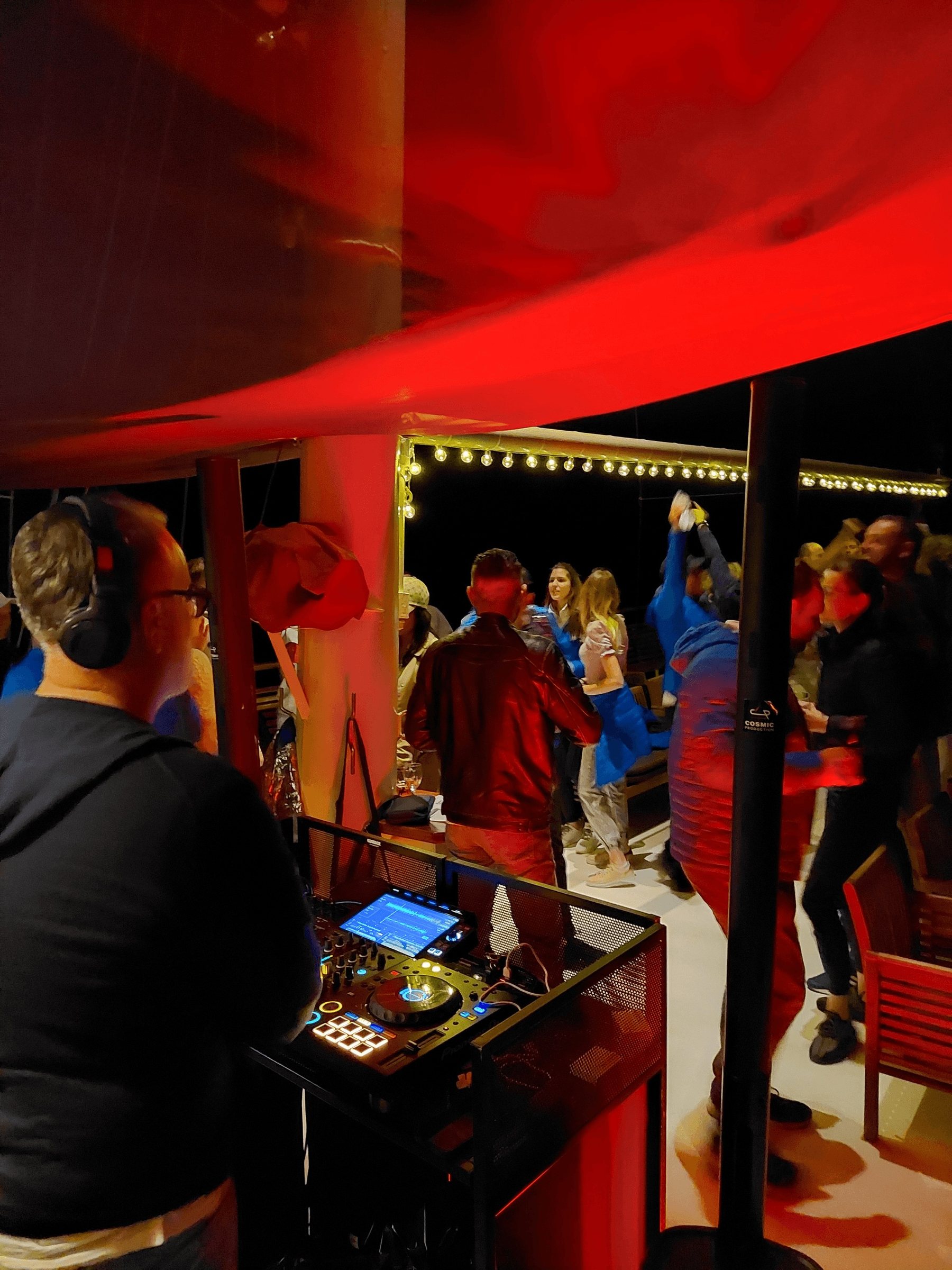 DJ mixing while guests dance under warm string lights at a night event on the deck of the yacht Polaris