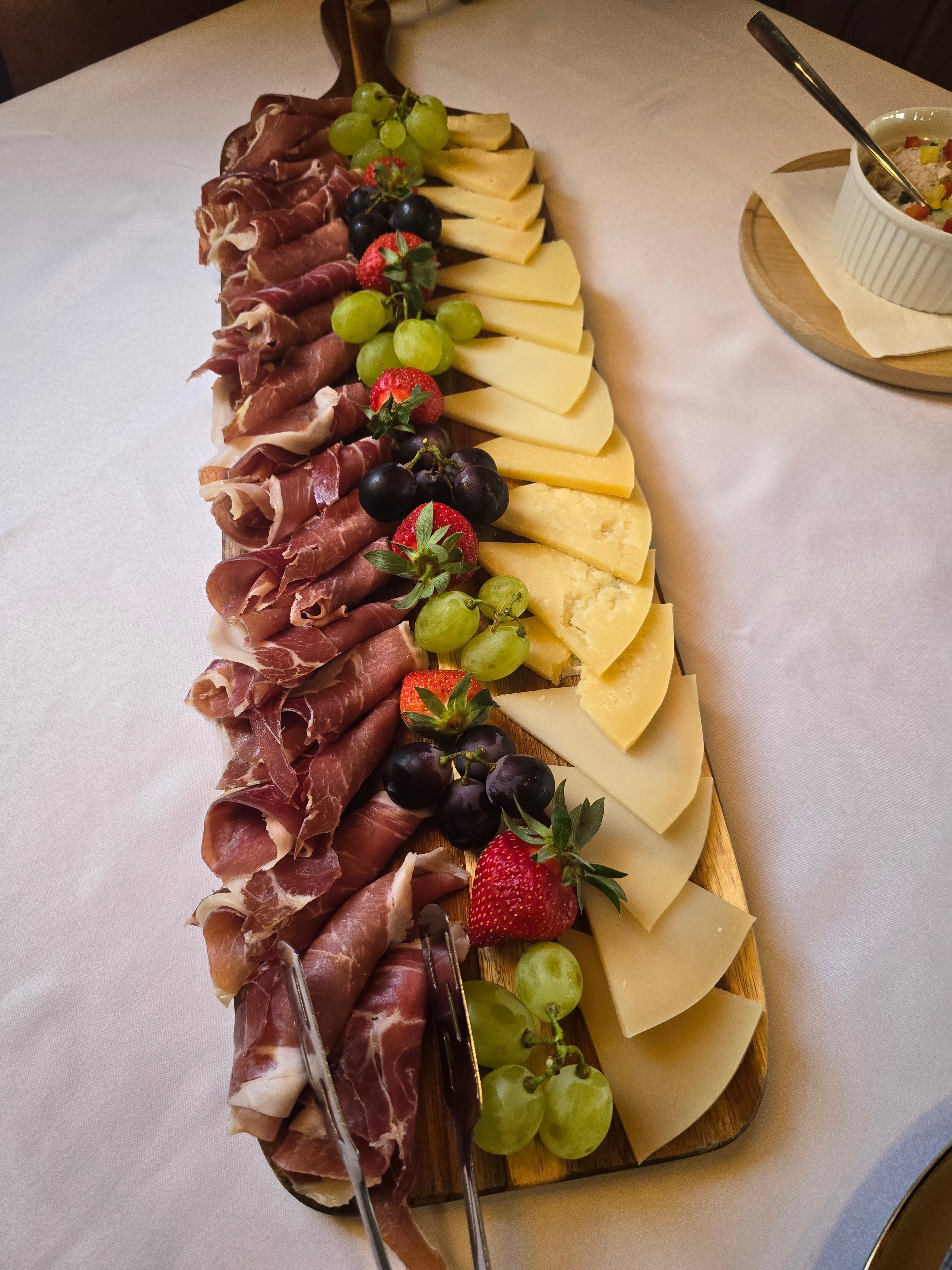 Wooden board of rolled Dalmatian prosciutto with assorted cheeses, grapes and strawberries