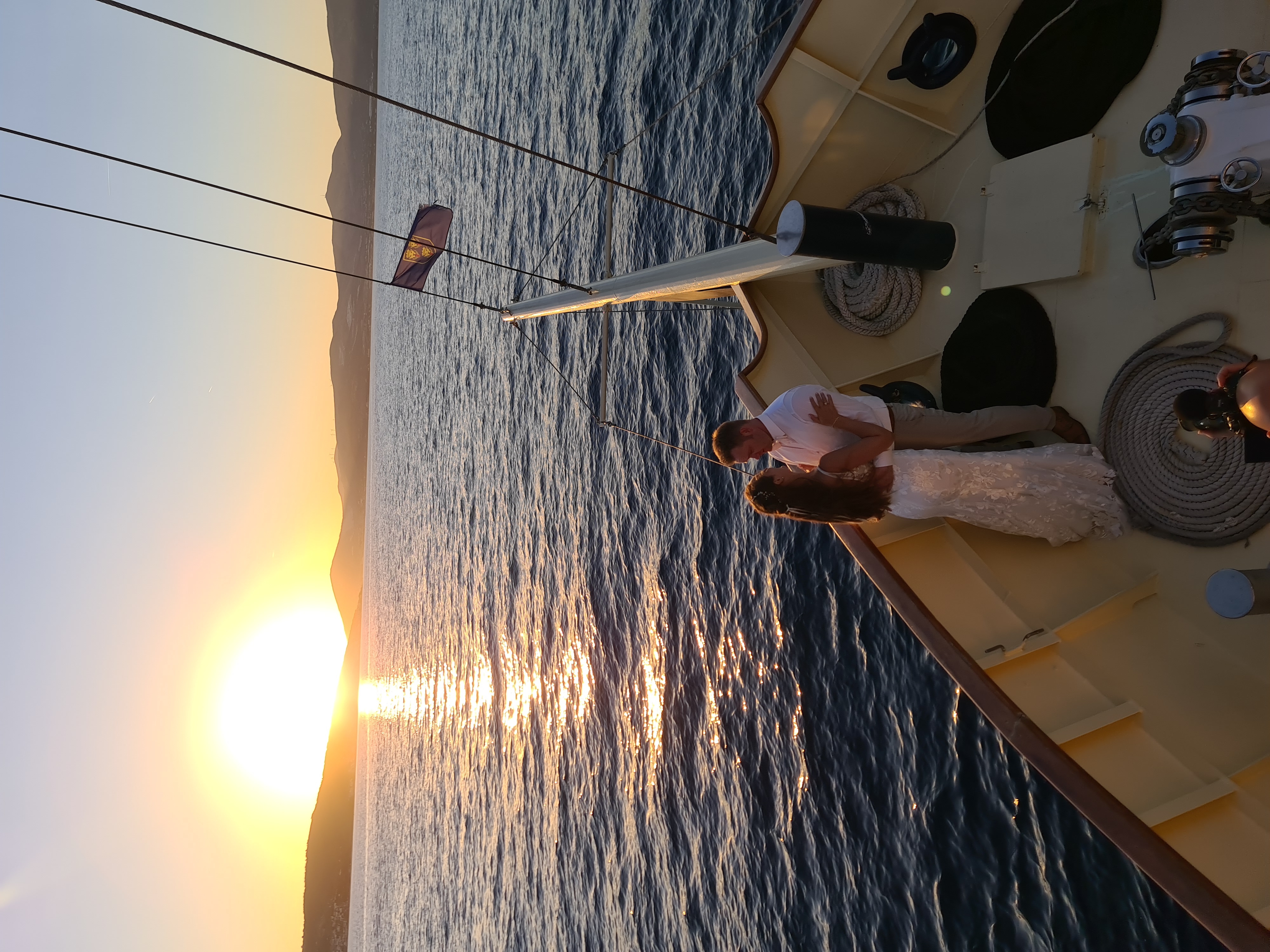 A bride and groom embracing at the bow of Polaris as the sun sets over the Adriatic