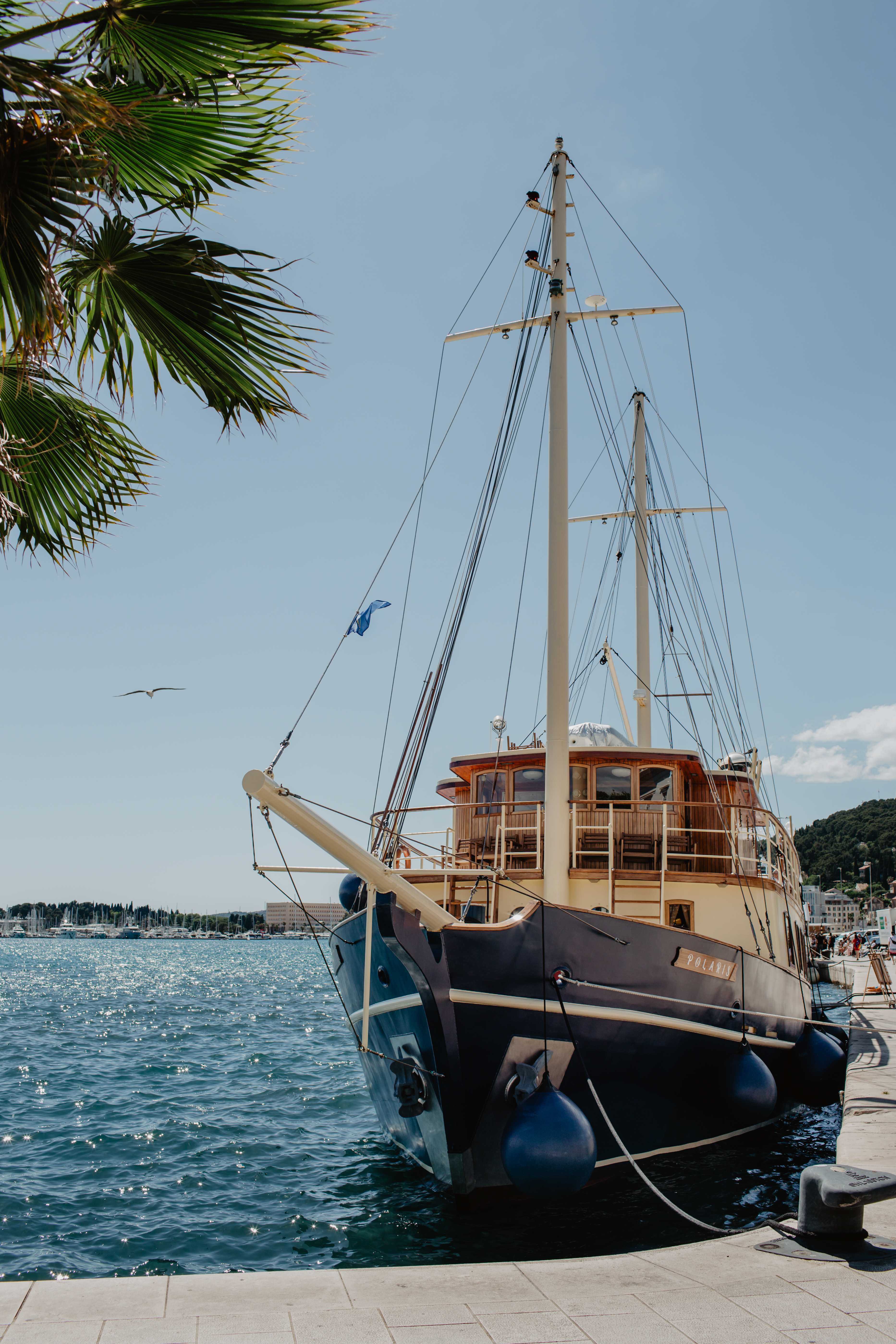 The classic yacht Polaris moored along the palm-lined Split waterfront promenade, ready for a private charter on the turquoise Adriatic
