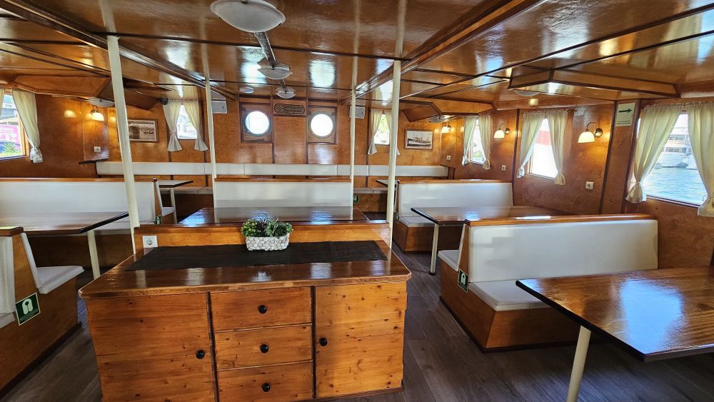 The warm, varnished-wood interior dining salon of Polaris with white cushioned booth seating, wooden tables and porthole windows