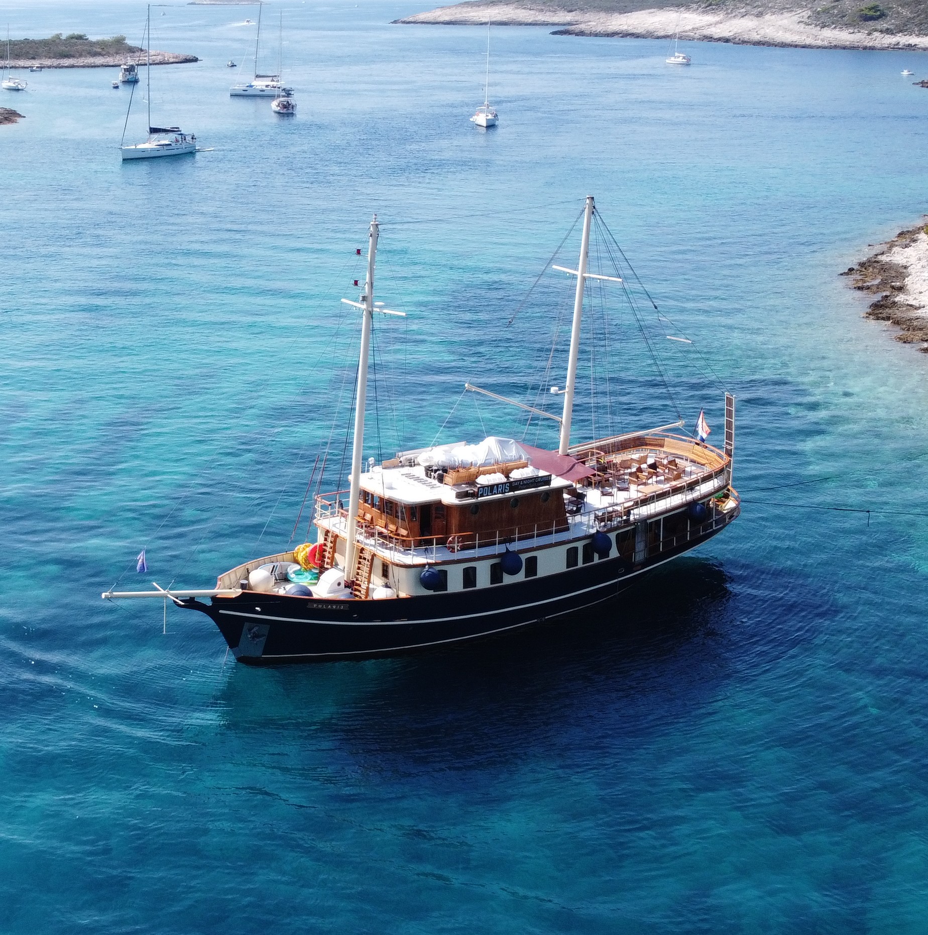 Die restaurierte Polaris heute, ein zweimastiges Holzschiff vor Anker im klaren türkisfarbenen Wasser der Adria