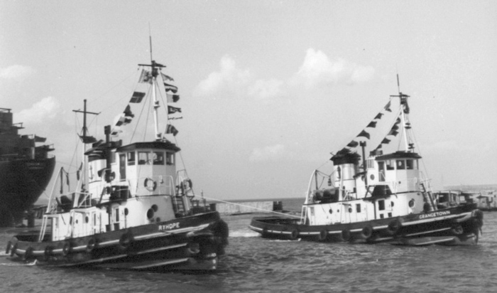 The tugs Ryhope and Grangetown dressed overall with signal flags in harbour beside a larger ship