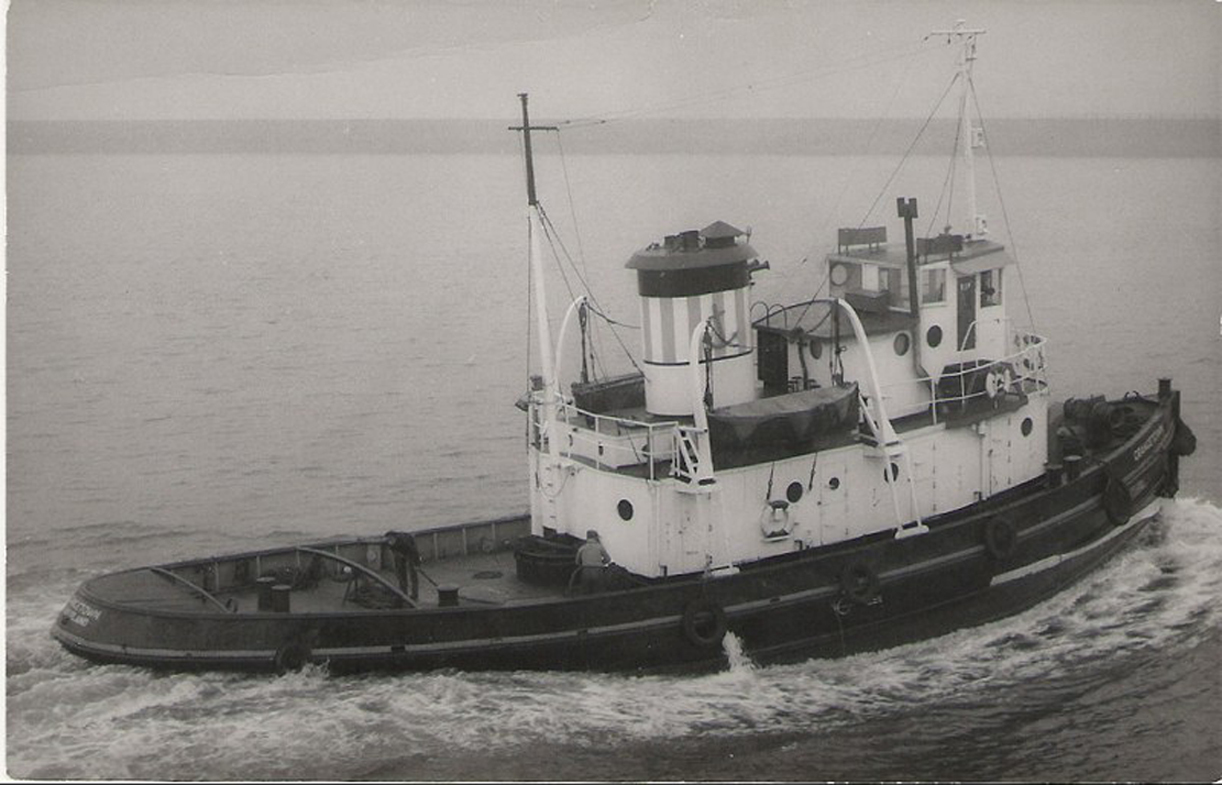 An elevated view of the tug Grangetown underway on calm water with crew working on deck