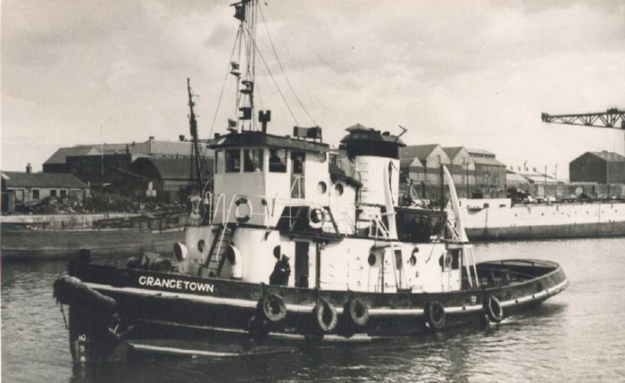 Der Schlepper Grangetown in einem Hafenbecken, dahinter Lagerhäuser und ein großer Kran am Kai