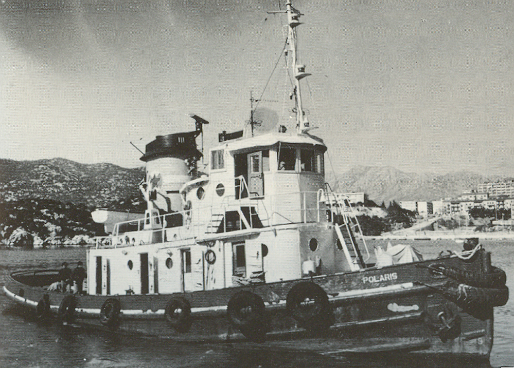 Vintage 1977 black-and-white photograph of the tugboat Polaris moored in the harbour of Ploče, with the Dalmatian hills and coastal town behind her