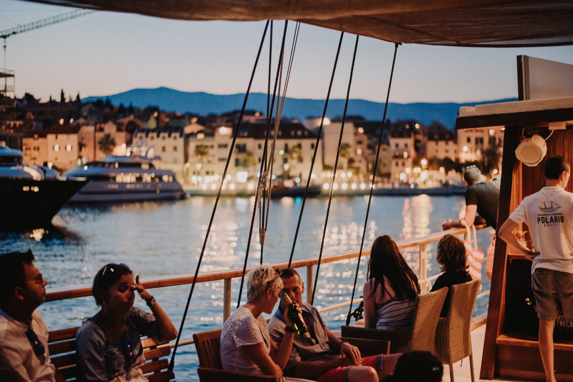 Guests relaxing on deck at dusk with the lights of Split behind