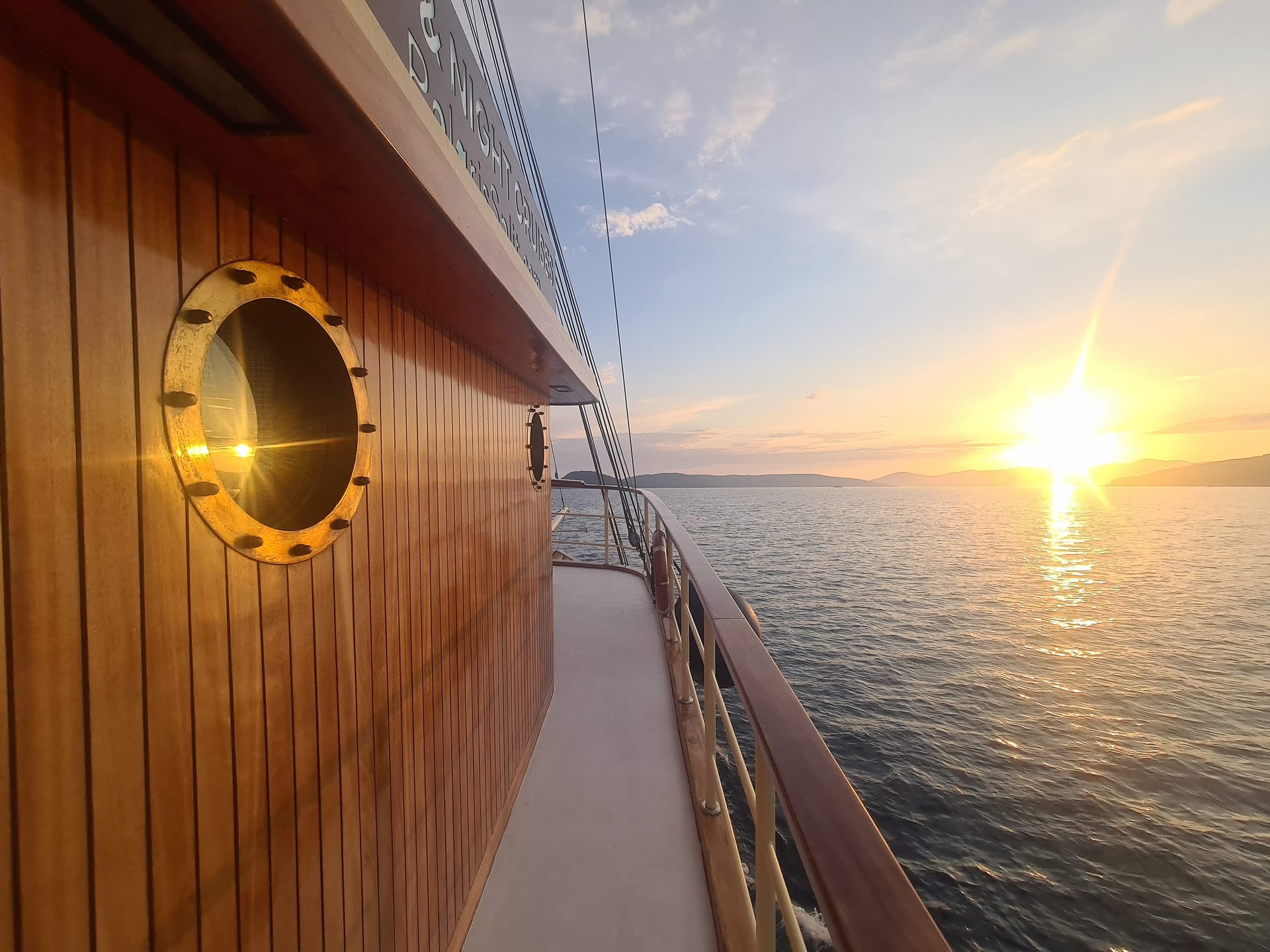Varnished wooden side deck and brass porthole with the sun low over the sea