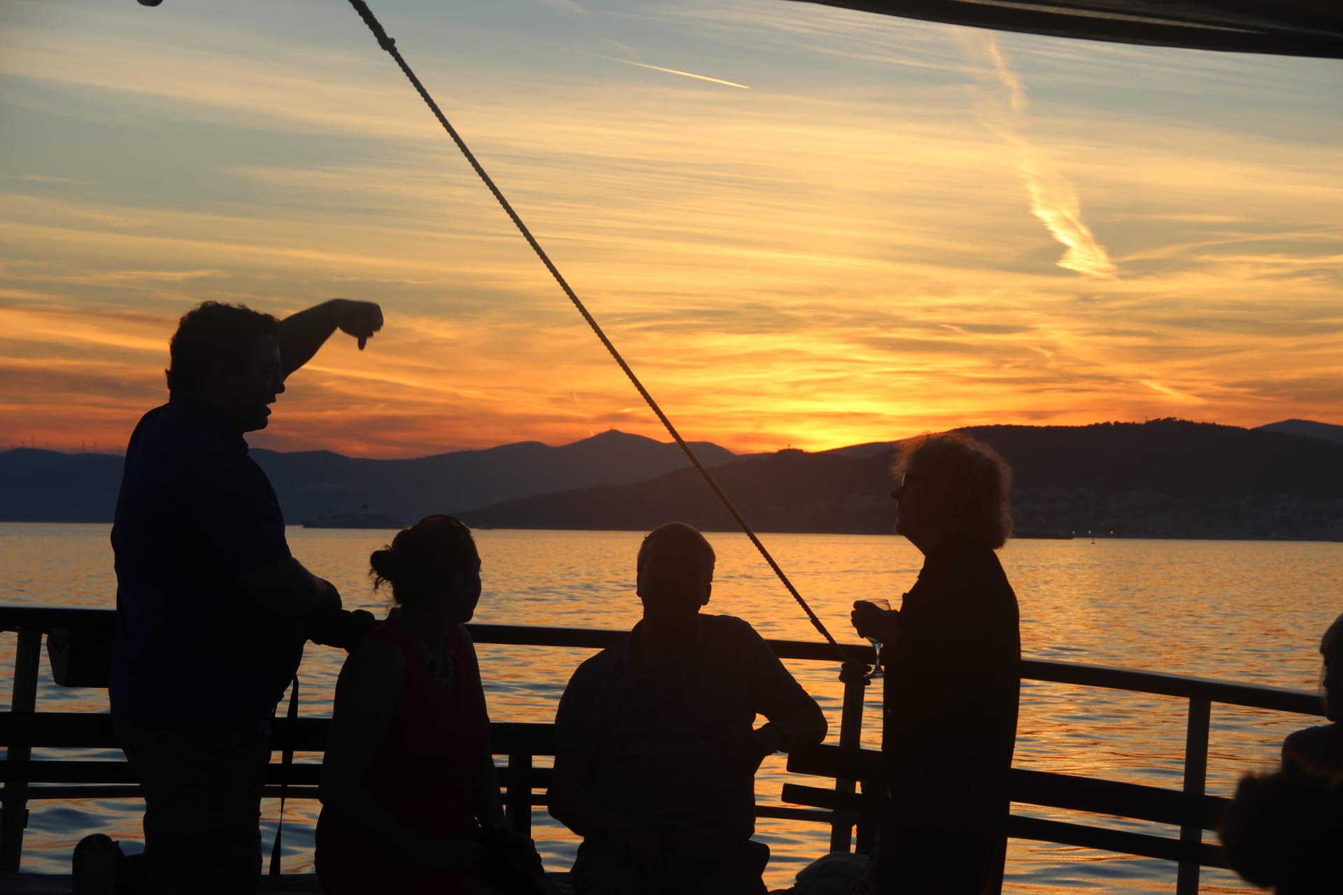 Guests chatting at the rail, silhouetted against a vivid orange sunset