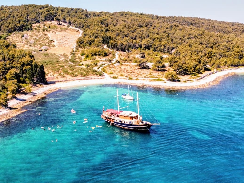 Aerial view of Polaris anchored in a secluded turquoise bay by a pebble beach