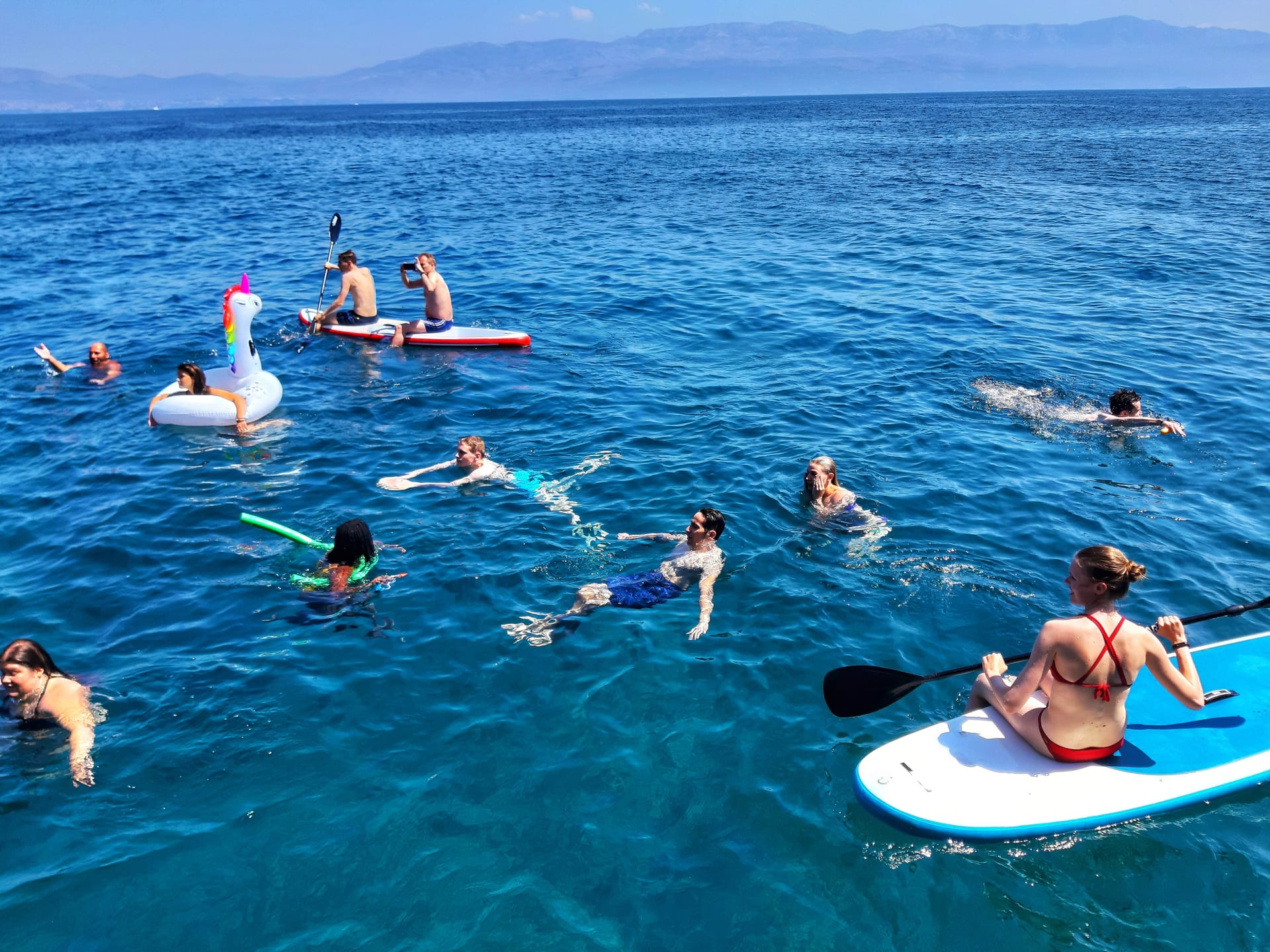 Swimmers and paddleboarders in the open sea with island mountains behind