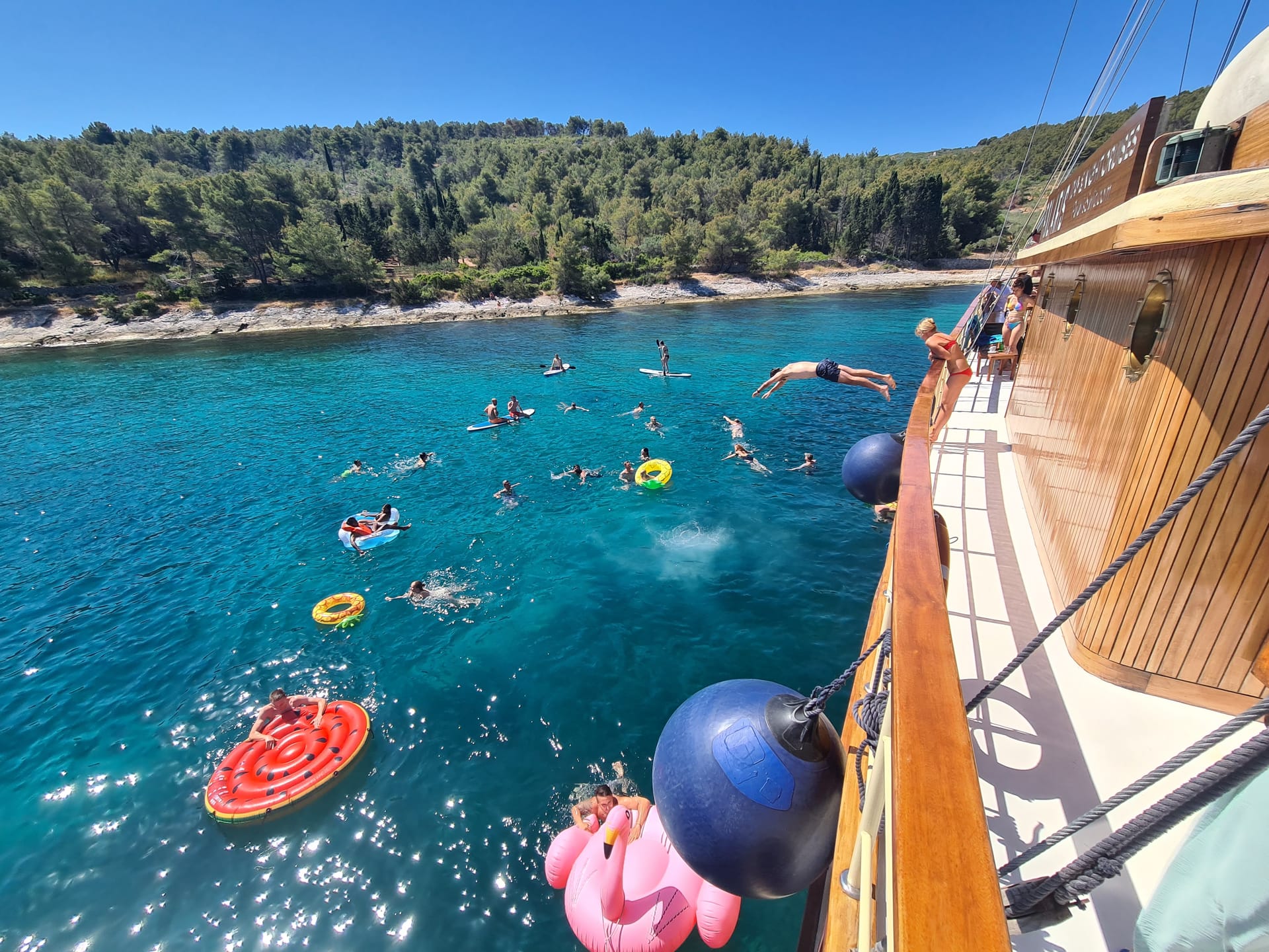 Guests swimming among colourful floats beside Polaris in a turquoise bay